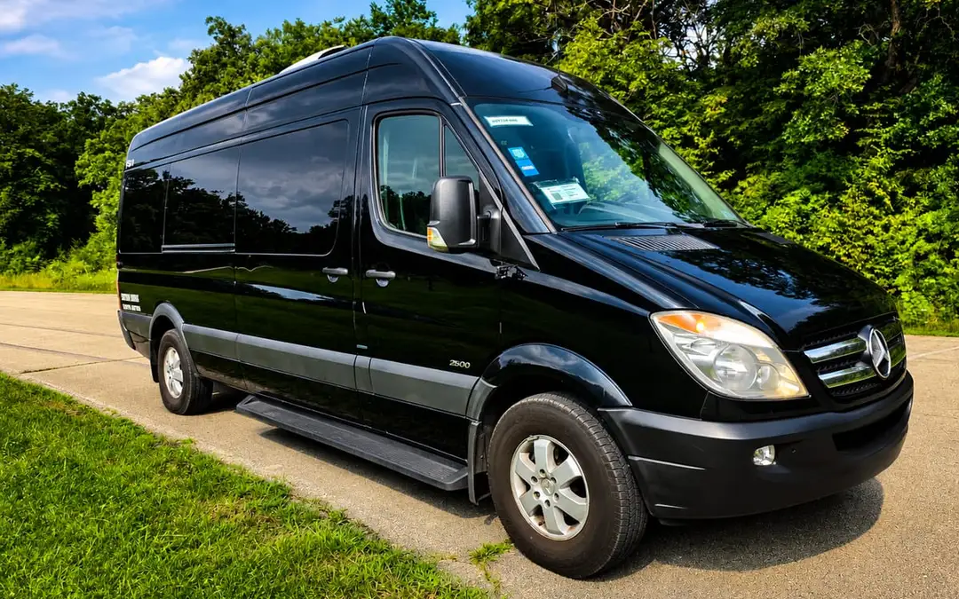 A black limo van parked on a quiet tree-lined road.